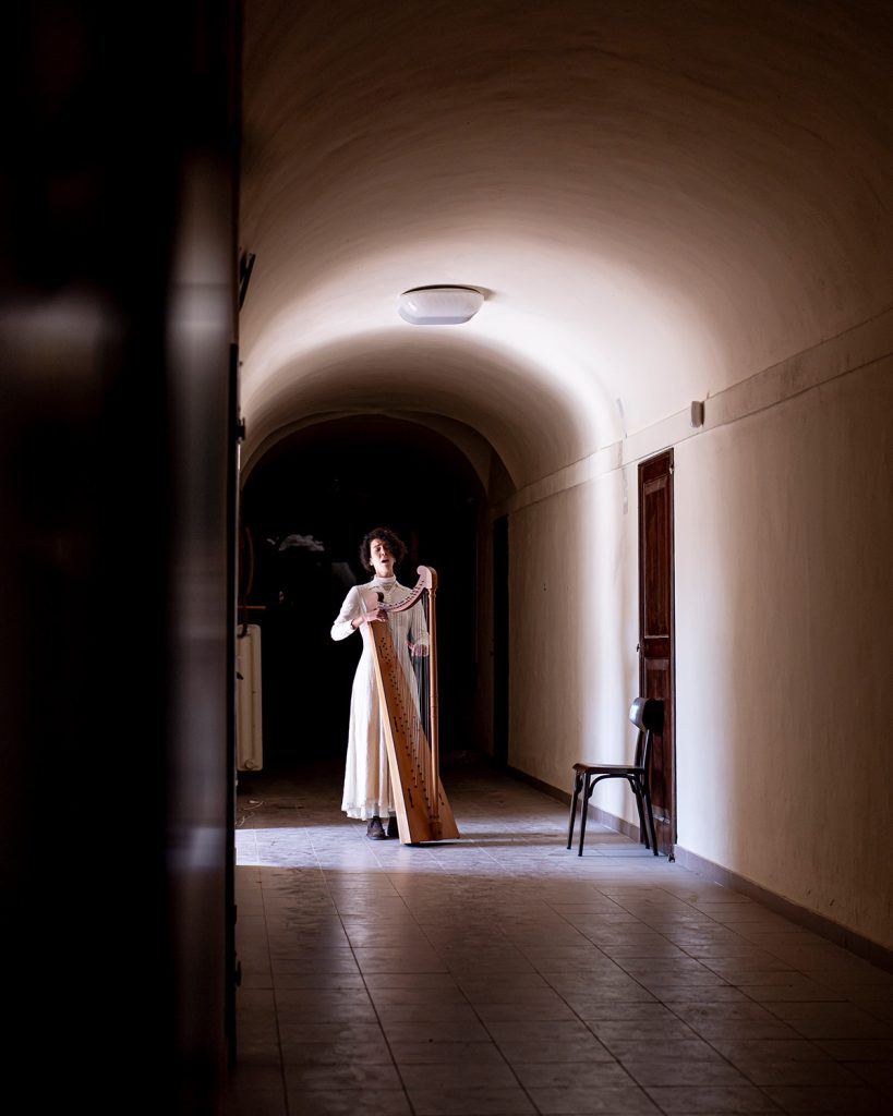 Una scena dell'opera ExClausura in cui una ragazza suona l'arpa all'interno di un corridoio del Monastero.